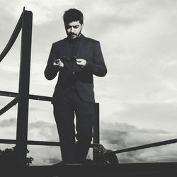 Handsome man holding sunglasses at observation point against sky