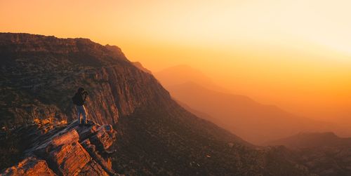 Scenic view of man on edge of a mountain against sky during sunset