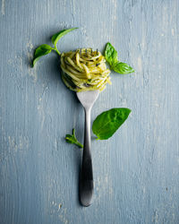 Cooked spaghetti on a fork, fresh basil leaves resembling a flower on rustic blue wooden background