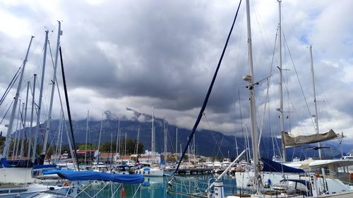 Sailboats moored in harbor against cloudy sky