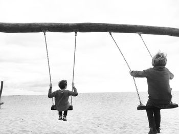 Rear view of boys swinging at sandy beach