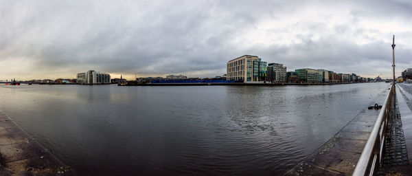 Buildings by river against sky in city