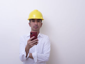 Portrait of young man holding camera against white background