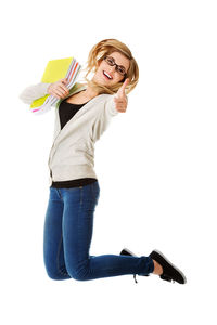 Smiling young woman holding spiral notebooks while jumping against white background