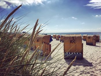 Hooded beach chairs on sand against sky