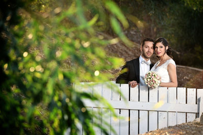 Portrait of wedding couple standing by fence
