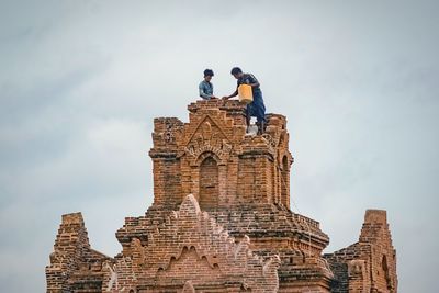 Low angle view of men standing on stack against sky