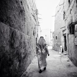 Rear view of man walking on road along buildings