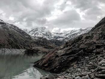 River by rocky mountains against cloudy sky during winter