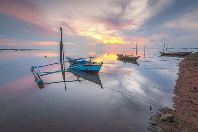 Boats moored on sea against sky during sunset