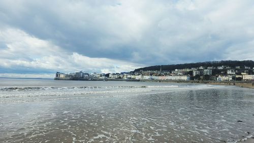 City at beach against cloudy sky