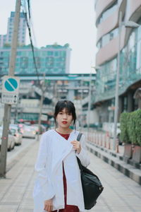 Portrait of young woman walking on sidewalk in city