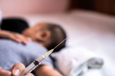 Cropped hand holding syringe with family in background