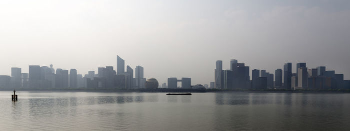 Sea by modern buildings against sky in city