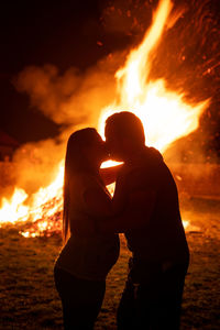 Silhouette couple kissing while standing against fire at night
