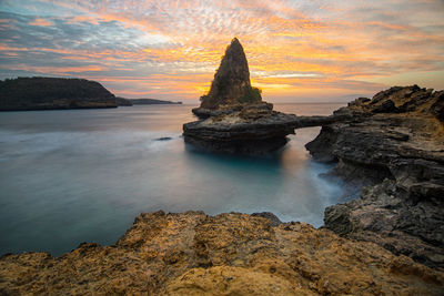 Rocks on sea shore against sky during sunset