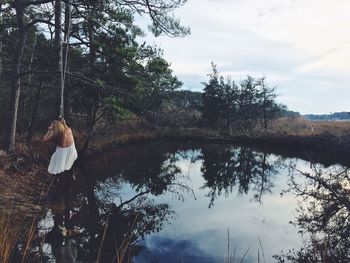 Rear view of woman standing by lake against sky