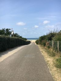 Empty road along plants and trees against sky