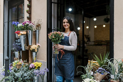 Young female florist holding flower vase while standing at shop