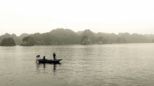 Silhouette people on boat in lake against sky