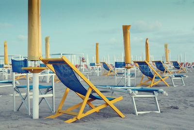 Chairs and tables on beach against sky