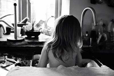 Rear view of girl sitting in kitchen sink