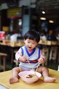 Girl with food in bowl sitting on table