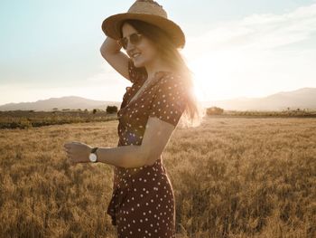 Side view of young woman standing on field against sky