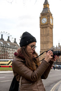 Woman photographing while standing against big ben