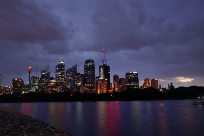 Illuminated buildings by river against sky at night