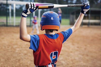 Rear view of boy holding baseball bat on field