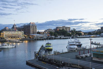 Boats in river by buildings in city against sky