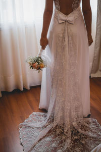 Low section of bride holding flower bouquet while standing at home