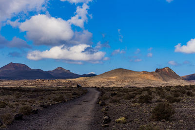 Dirt road leading towards mountains against sky