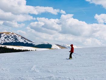 Skier on the slope surrounded by snowcapped mountains on a day with blue sky and fluffy clouds