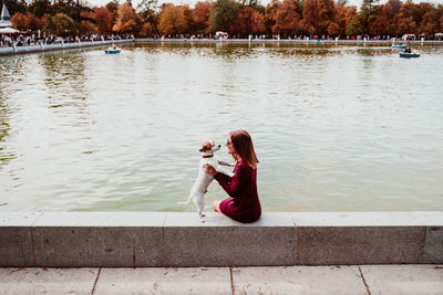 Side view of woman with dog sitting by lake