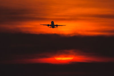 Silhouette airplane flying against orange sky