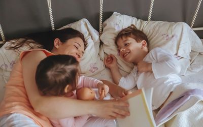 High angle view of mother telling bed time story to children on bed at home