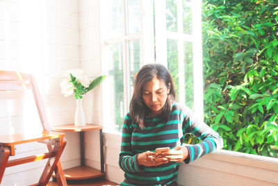Young woman using phone while sitting on table