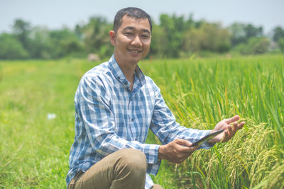 Portrait of smiling farmer with digital tablet holding crops on field