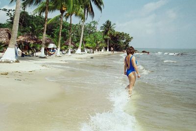 Full length of shirtless man standing on beach against sky