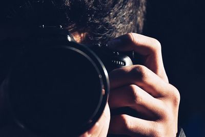 Close-up of man photographing with digital camera against black background