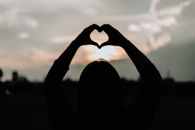 Silhouette woman with heart shape against sky during sunset