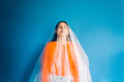 Woman covered in plastic standing against blue background