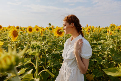 Portrait of young woman standing amidst sunflowers against sky