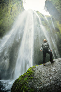Man standing on rock looking at waterfall
