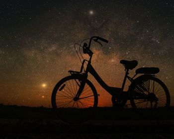 Silhouette bicycle on field against sky at night