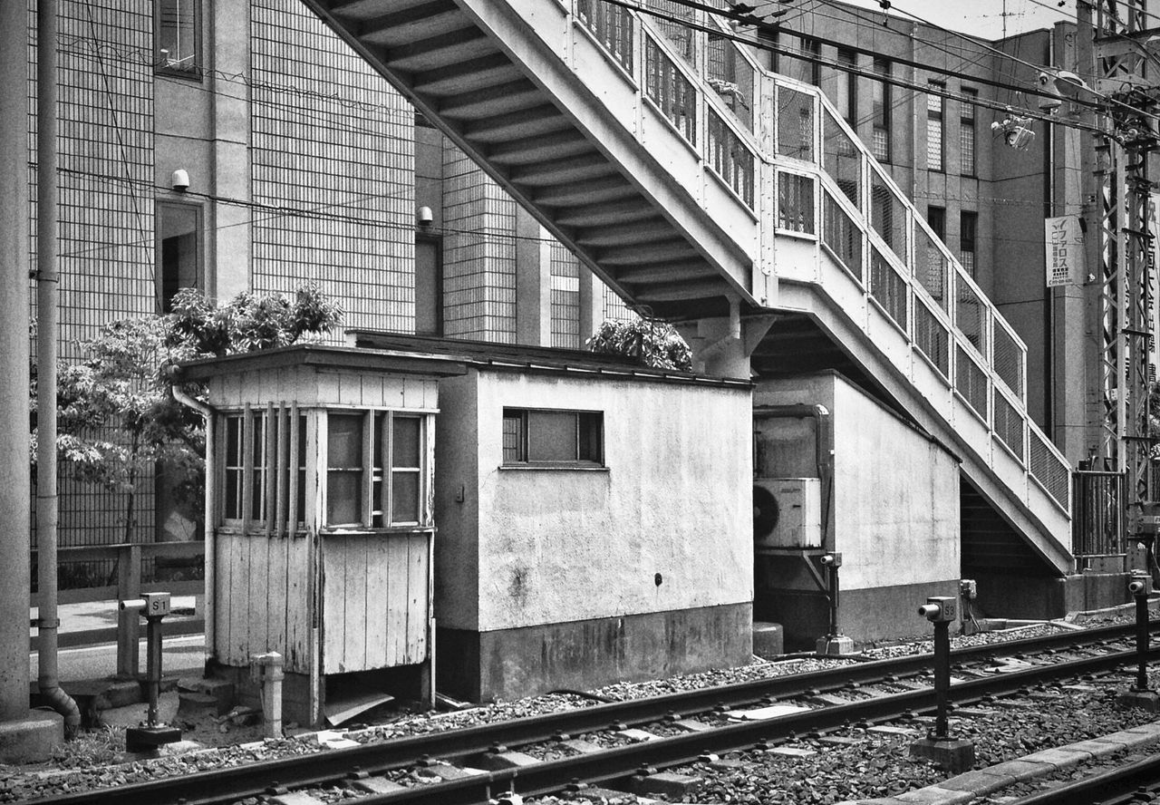 architecture, building exterior, built structure, window, residential building, railing, residential structure, building, house, railroad track, city, day, outdoors, no people, metal, fence, tree, rail transportation, connection, sunlight