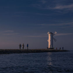 People on sea against sky during sunset