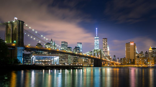 Illuminated modern buildings by river against sky in city at night